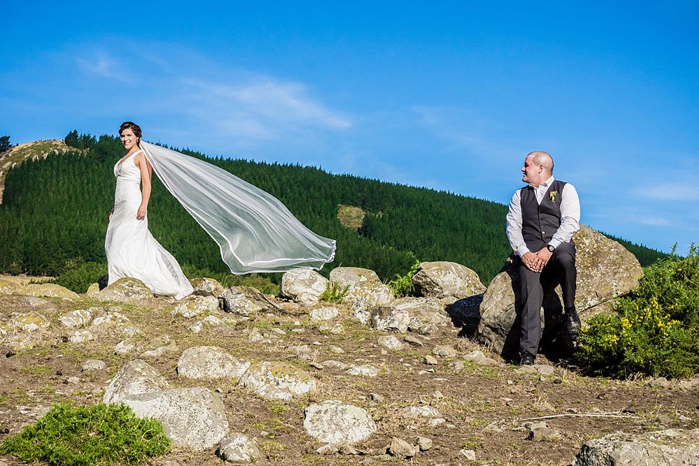 Bride and groom on a hilltop on a windy day with veil playing in the wind and groom looking at bride outside Cossars Wineshed Wedding venue 