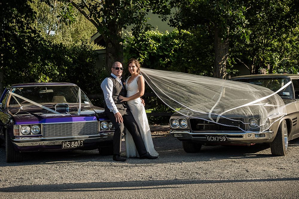 Bride and groom standing between two cars at the wedding venue