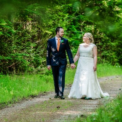 Pip and Oz capture a photo of bride and groom walking along a forest path, in Hanmer Springs